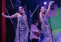 two women in silver dresses singing on stage