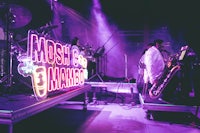 a group of musicians on stage with a neon sign