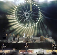 a group of people on stage with a large wheel in the background